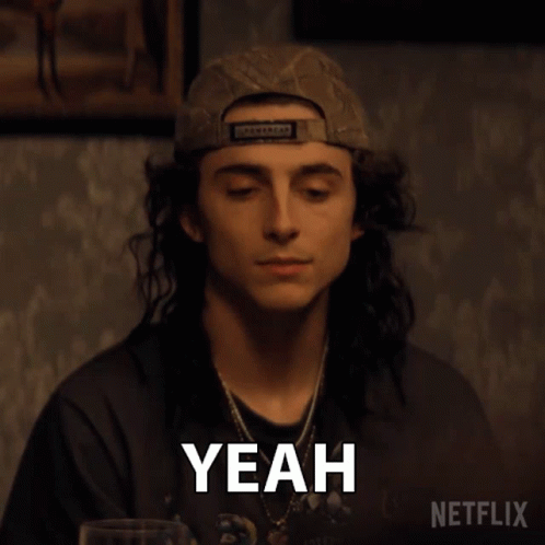 A Man With Long Hair Is Wearing A Baseball Cap And Making A Yeah Gesture . GIF
