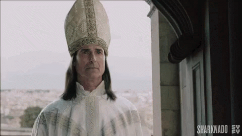 A Man With Long Hair Is Wearing A Bishop 'S Hat And Robe . GIF