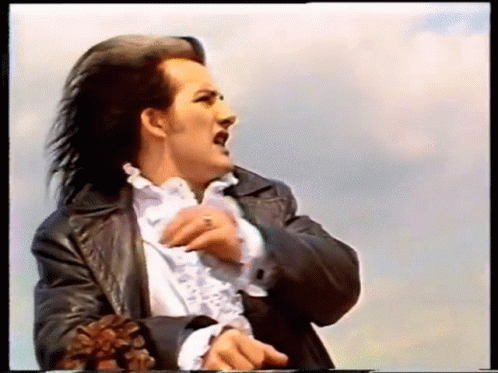 A Man With Long Hair Is Wearing A Black Leather Jacket And White Shirt GIF