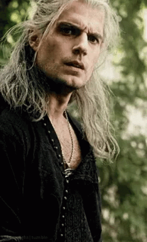 a man with long hair is wearing a black shirt and a necklace .