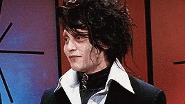 A Man With Long Hair Is Wearing A Black Suit And A White Collar . GIF