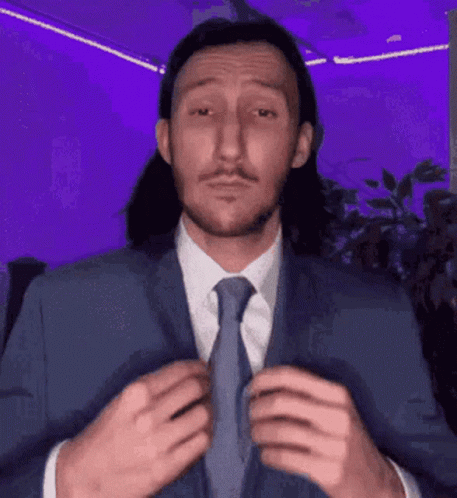 A Man With Long Hair Is Wearing A Suit And Tie GIF