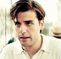 A Man With Long Hair Is Wearing A White Shirt And Looking At The Camera . GIF