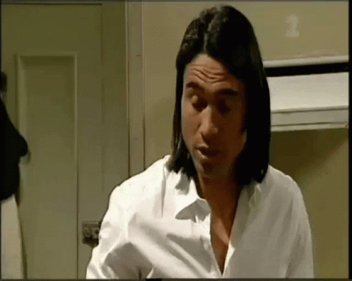 A Man With Long Hair Is Wearing A White Shirt And Looking Down . GIF