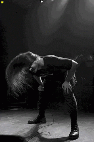 A Man With Long Hair Singing Into A Microphone On Stage GIF