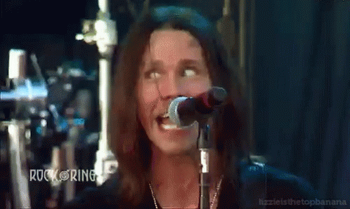 a man with long hair singing into a microphone with rock ring written on the bottom left
