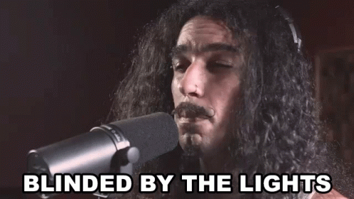 A Man With Long Hair Singing Into A Microphone With The Words Blinded By The Lights Below Him GIF