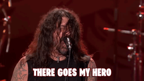 A Man With Long Hair Singing Into A Microphone With The Words " There Goes My Hero " Above Him GIF