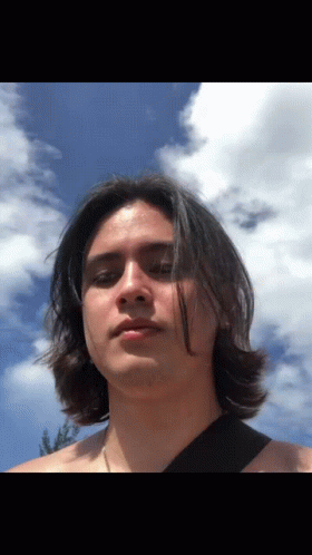 A Man With Long Hair Stands In Front Of A Blue Sky With Clouds GIF