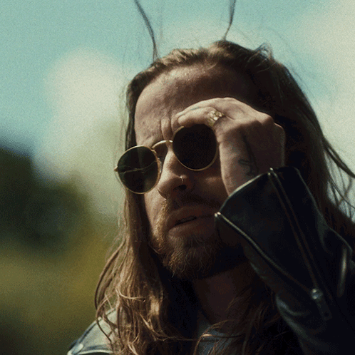 A Man With Long Hair Wearing Sunglasses Has A Tattoo On His Arm GIF