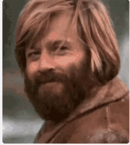 A Man With Long Red Hair And A Beard Looks At The Camera . GIF