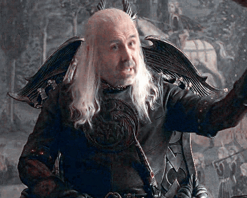 A Man With Long White Hair And A Beard Is Sitting In A Chair With His Arm Outstretched GIF