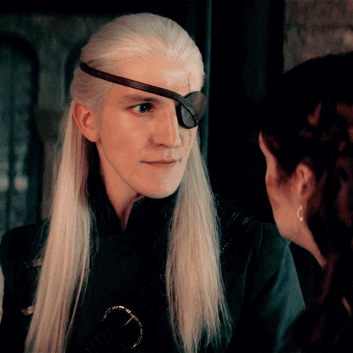A Man With Long White Hair And An Eye Patch On His Forehead Looks At A Woman GIF