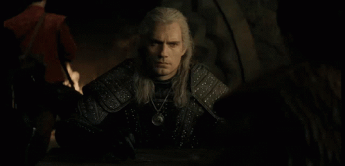 a man with long white hair is sitting at a table with a necklace around his neck