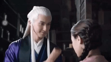 a man with long white hair is standing next to a woman in a purple dress .