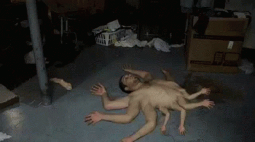 A Man With Many Hands Is Laying On The Floor In A Basement . GIF