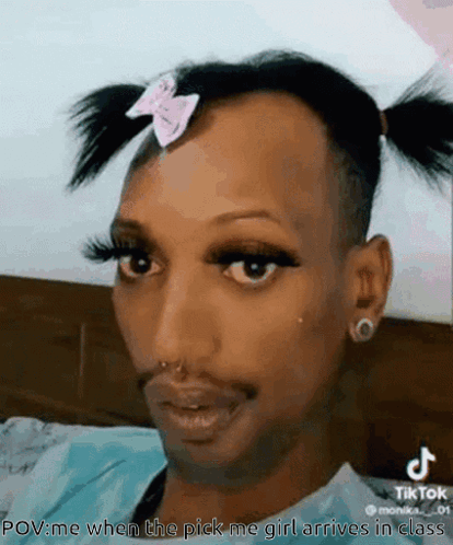 a man with pigtails and a pink bow on his head is wearing makeup .