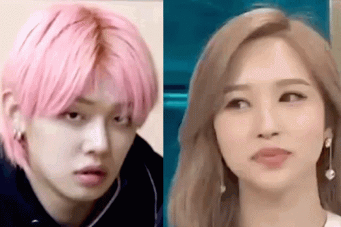 A Man With Pink Hair And A Woman With Blonde Hair Are Standing Next To Each Other And Looking At Each Other . GIF