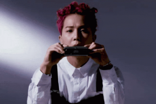 A Man With Pink Hair Is Holding A Black Object In Front Of His Mouth GIF