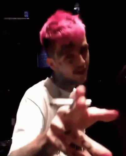 A Man With Pink Hair Is Making A Funny Face While Holding A Cell Phone In A Dark Room . GIF