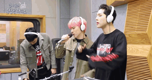A Man With Pink Hair Is Singing Into A Microphone While Another Man Looks On GIF
