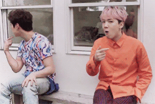 A Man With Pink Hair Is Sitting Next To Another Man In An Orange Shirt GIF