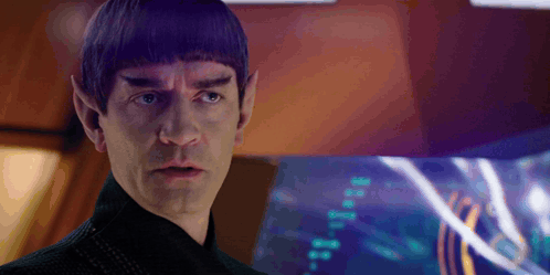 a man with purple hair and ears is standing in front of a computer screen