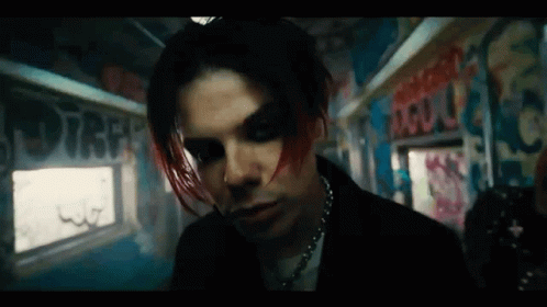 a man with red hair and black makeup is standing in a room with graffiti on the wall .