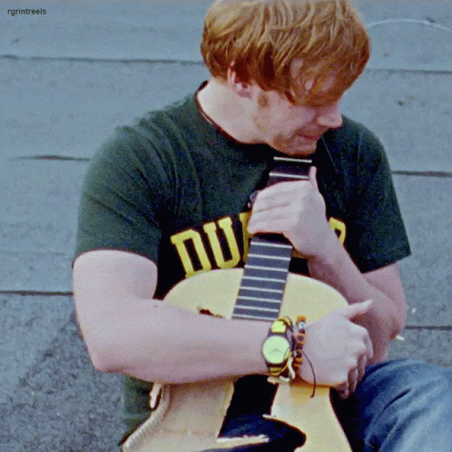 A Man With Red Hair Is Playing A Guitar And Wearing A Shirt That Says Nu GIF