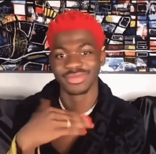 A Man With Red Hair Is Sitting In Front Of A Painting And Making A Face . GIF