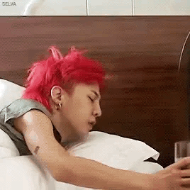 A Man With Red Hair Is Sleeping On A Bed While Looking At His Phone . GIF