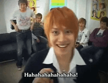 A Man With Red Hair Is Smiling In Front Of A Group Of People In A Room . GIF