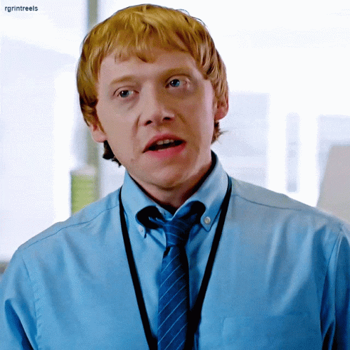A Man With Red Hair Is Wearing A Blue Shirt And Tie With A Lanyard Around His Neck .. GIF