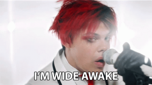 a man with red hair singing into a microphone with the words " i 'm wide awake " behind him