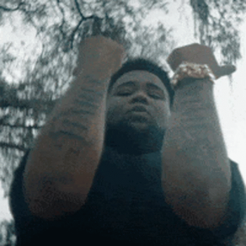 A Man With Tattoos On His Arms Is Holding His Fist Up In The Air . GIF