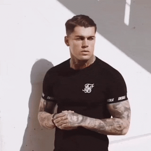A Man With Tattoos On His Arms Is Wearing A Black Siksilk T-Shirt . GIF