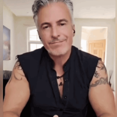 A Man With Tattoos On His Arms Is Wearing A Black Vest GIF