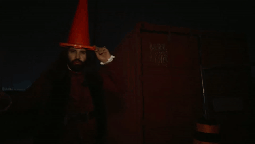 A Man With Vampire Teeth Wearing An Orange Cone Hat GIF
