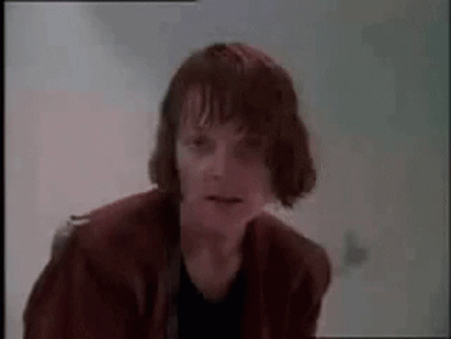A Man With Wet Hair Is Standing In Front Of A White Wall And Making A Funny Face . GIF