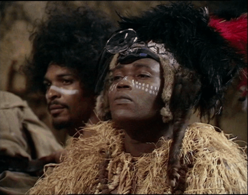 A Man With White Paint On His Face And A Feathered Headdress GIF