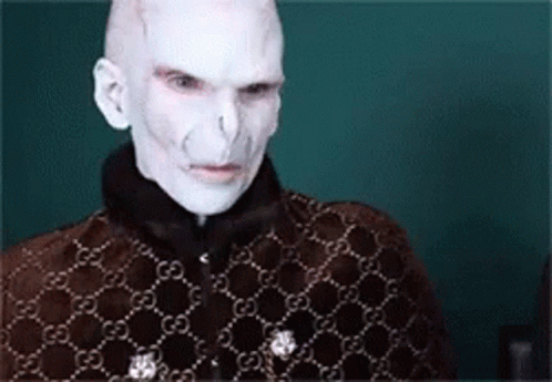A Man With White Paint On His Face Is Wearing A Brown Jacket With A Gucci Pattern . GIF