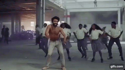 A Man Without A Shirt Is Dancing In A Parking Garage With A Group Of People . GIF