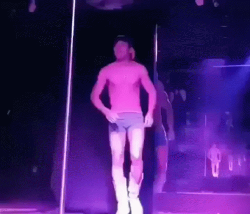 a man without a shirt is dancing on a pole in a dark room