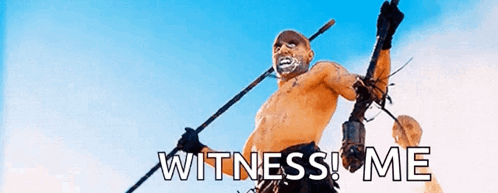 A Man Without A Shirt Is Holding A Spear With The Words Witness Me Written On It . GIF
