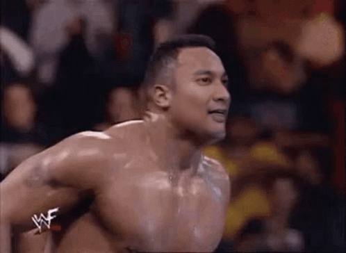 A Man Without A Shirt Is Jumping In The Air While Wearing A Wrestler 'S Belt . GIF