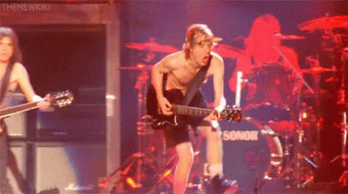 A Man Without A Shirt Is Playing A Guitar On Stage In Front Of A Drum Set . GIF