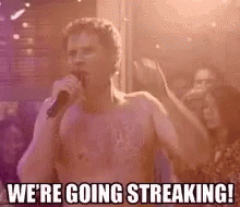 A Man Without A Shirt Is Singing Into A Microphone In Front Of A Crowd . GIF