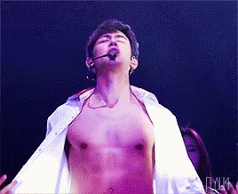 A Man Without A Shirt Is Singing Into A Microphone On A Stage GIF