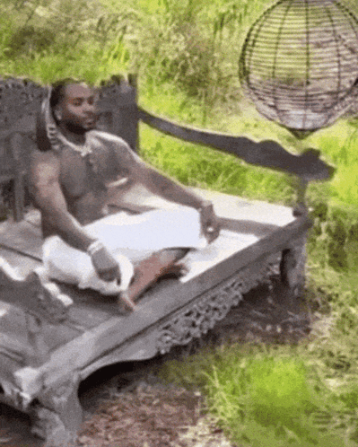 A Man Without A Shirt Is Sitting On A Wooden Bench In The Woods . GIF