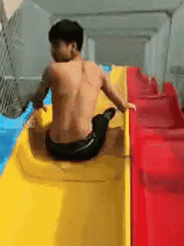 A Man Without A Shirt Is Sitting On A Yellow And Red Slide GIF